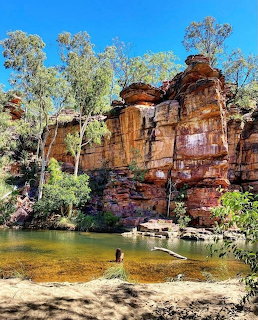 Sandstone rock cliffs with eucalyptus trees surrounding a calm waterhole in the Australian outback