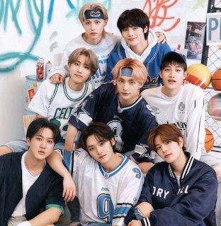 Eight young men from Stray Kids posing together in sporty jerseys with basketballs in background
