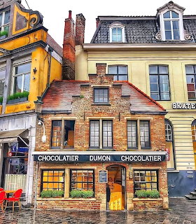 Historic brick chocolatier shop with ornate facade on wet cobblestone street flanked by colorful buildings