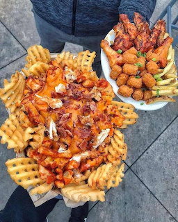 Hands holding trays of loaded waffle fries with bacon and cheese, plus fried finger foods