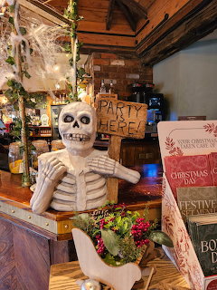 White skeleton figure with wreath in decorated rustic room with wooden beams and holiday items