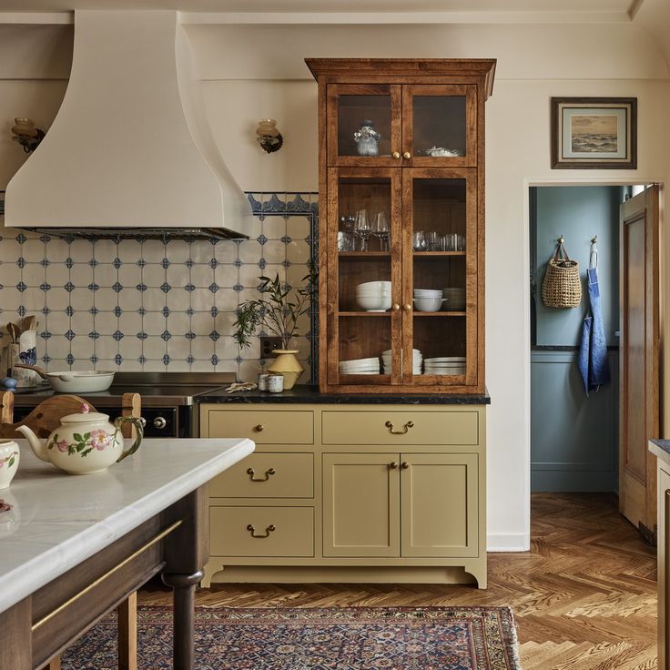 Traditional kitchen interior with cream cabinetry, wooden cupboard, tiled wall, and patterned rug
