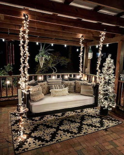 Illuminated porch swing with Christmas lights and decorated trees on wooden deck at night