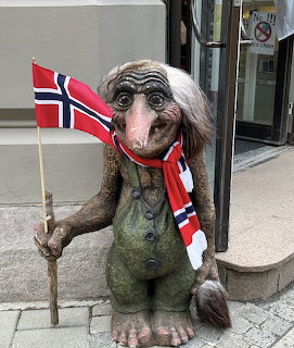 Troll statue with white hair holding Norwegian flags and walking stick on urban street