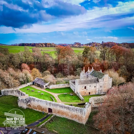 Aerial view of a stone castle with surrounding walls, trees, and green countryside