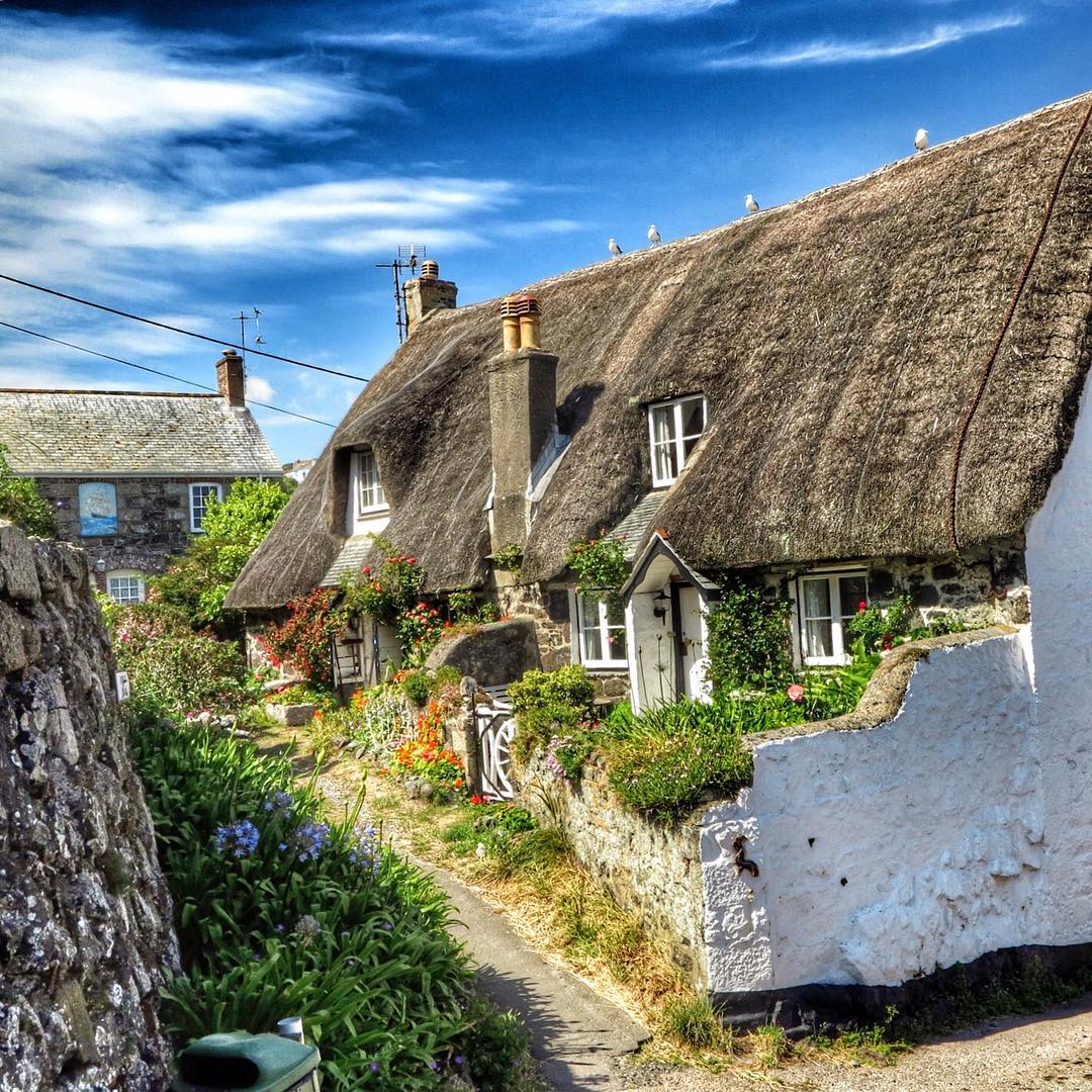 White cottage with thatched roof and garden path on sunny day