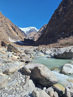 Turquoise glacial river flowing through a rocky valley with snow-capped mountain peaks in the background