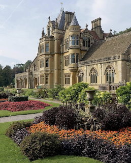 Victorian Gothic mansion with tower and ornate stonework surrounded by formal gardens with vibrant flowerbeds