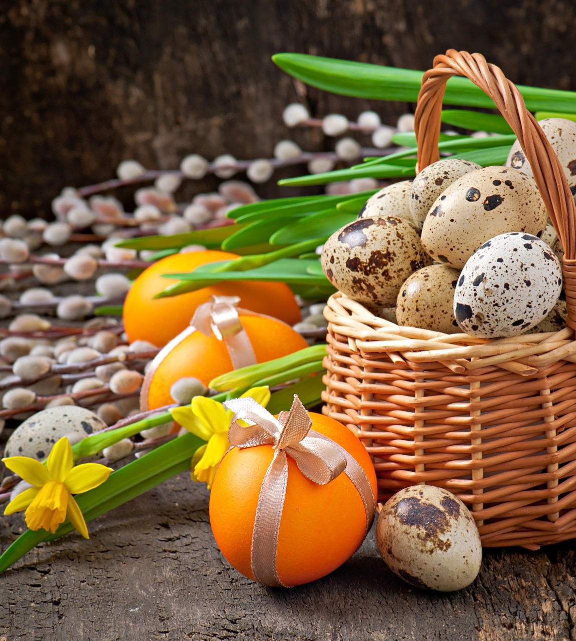 Wicker basket of speckled eggs with orange tulips and yellow daffodils on wood