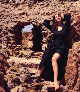 Woman in black dress posing among rocky ruins with arms raised in warm sunlight