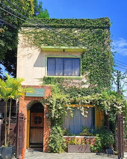 Two-story building facade covered in green ivy and white flowering vines with an arched wooden door