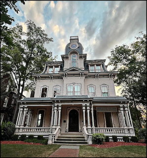 Large old Victorian house with porch and trees under a cloudy sky