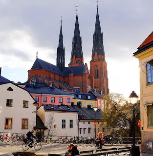 Uppsala Cathedral with tall dark spires towering over colorful historic buildings and a street with cyclists