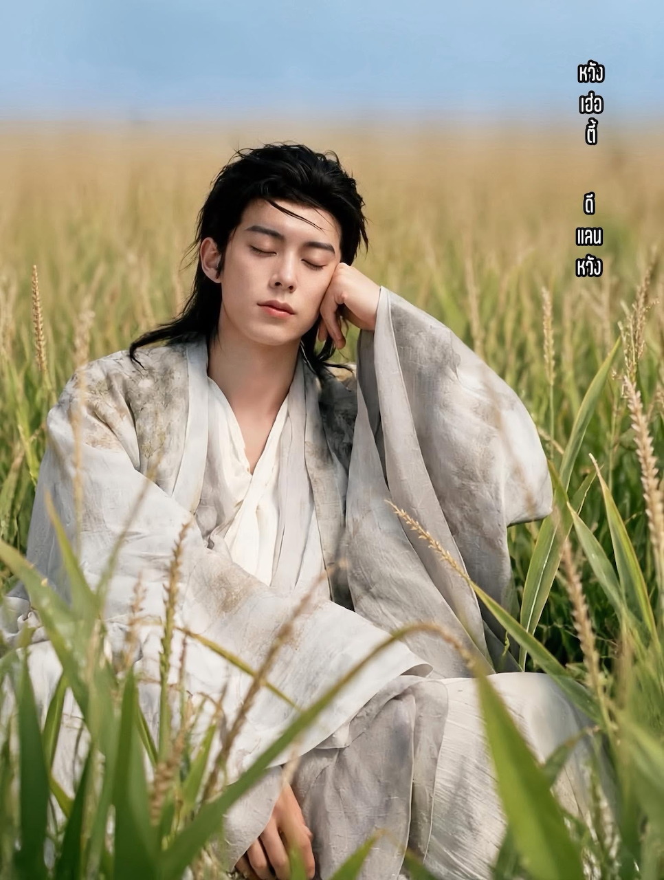 Young man in white traditional robe sitting in tall grass with eyes closed