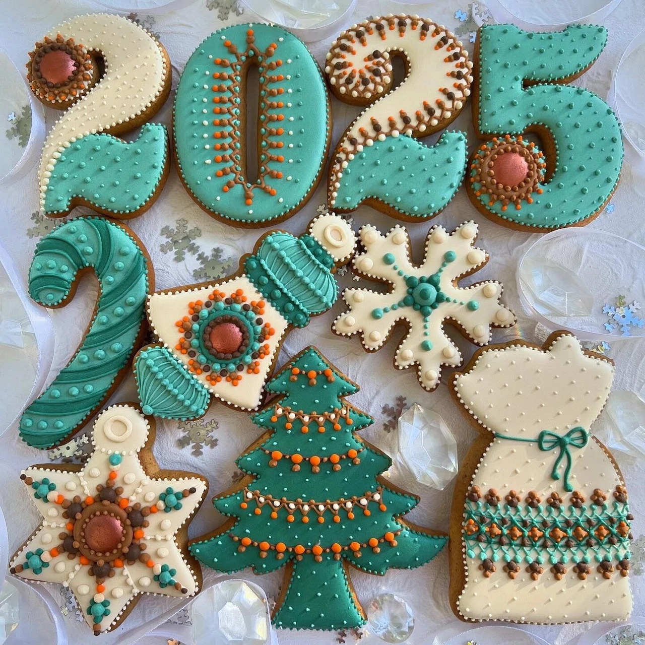 Assorted knitted Christmas ornaments arranged on white fabric, featuring 2025 numbers and holiday shapes in teal and beige