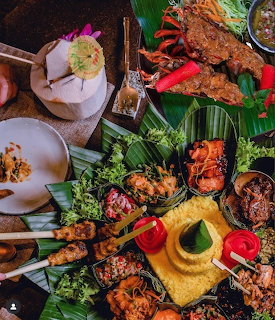 Overhead view of assorted Indonesian dishes with satay, grilled fish, rice, and vegetables on banana leaves