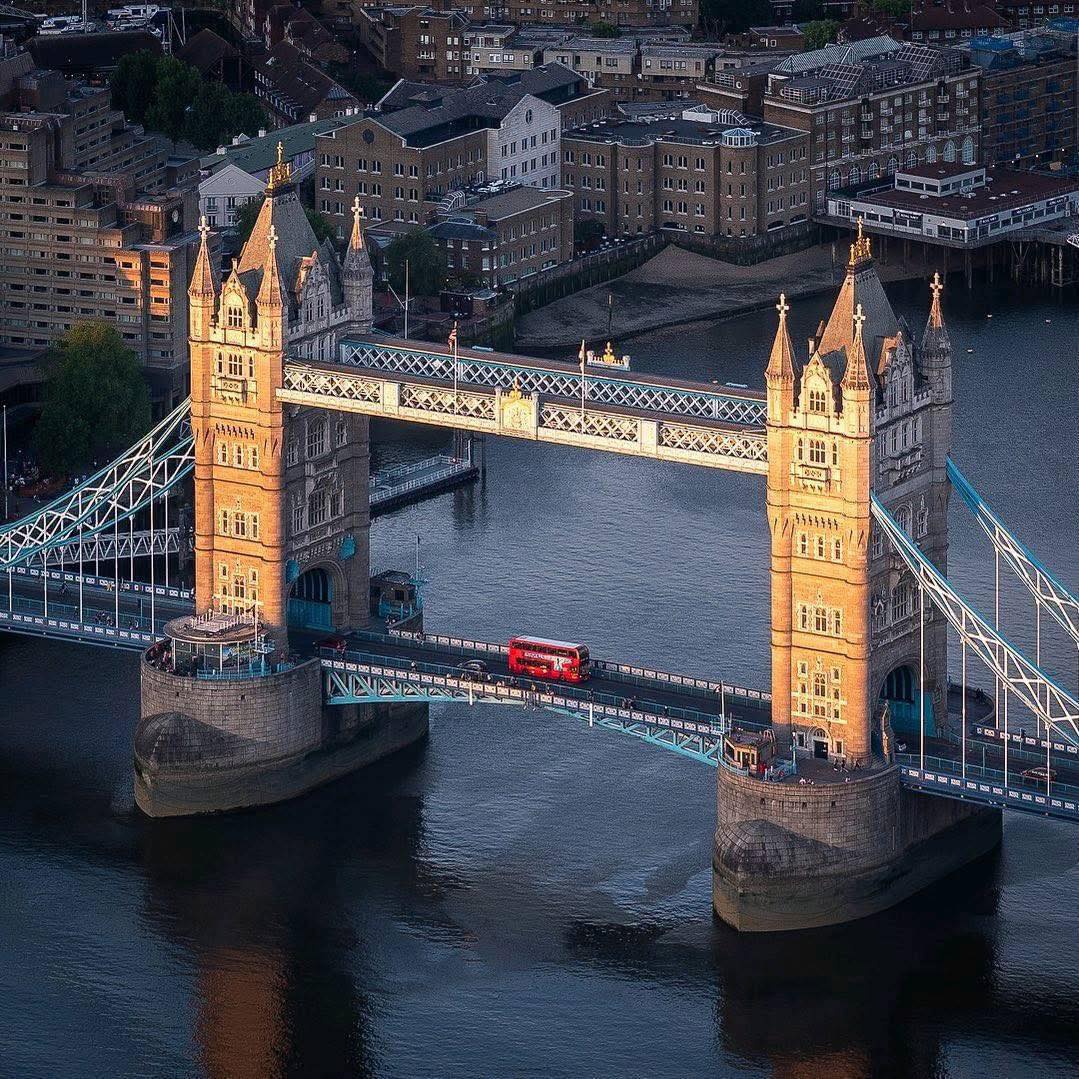Aerial view of Tower Bridge over River Thames in London at dusk with illuminated towers and red bus crossing