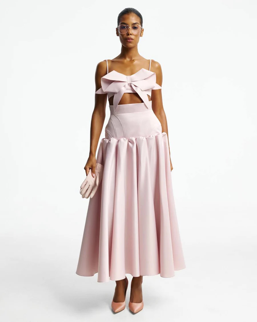Woman in a pale pink off-shoulder bow top gown with a full skirt, posing in a studio