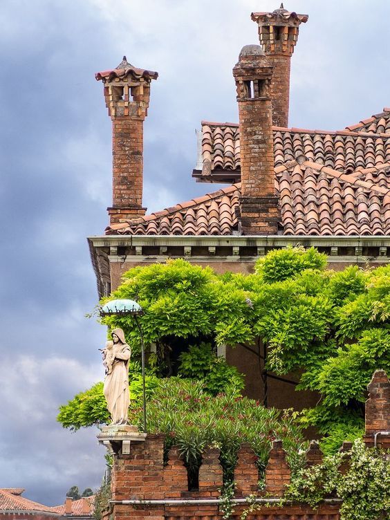 Terracotta rooftop with brick chimneys, ivy-covered wall, and a stone statue