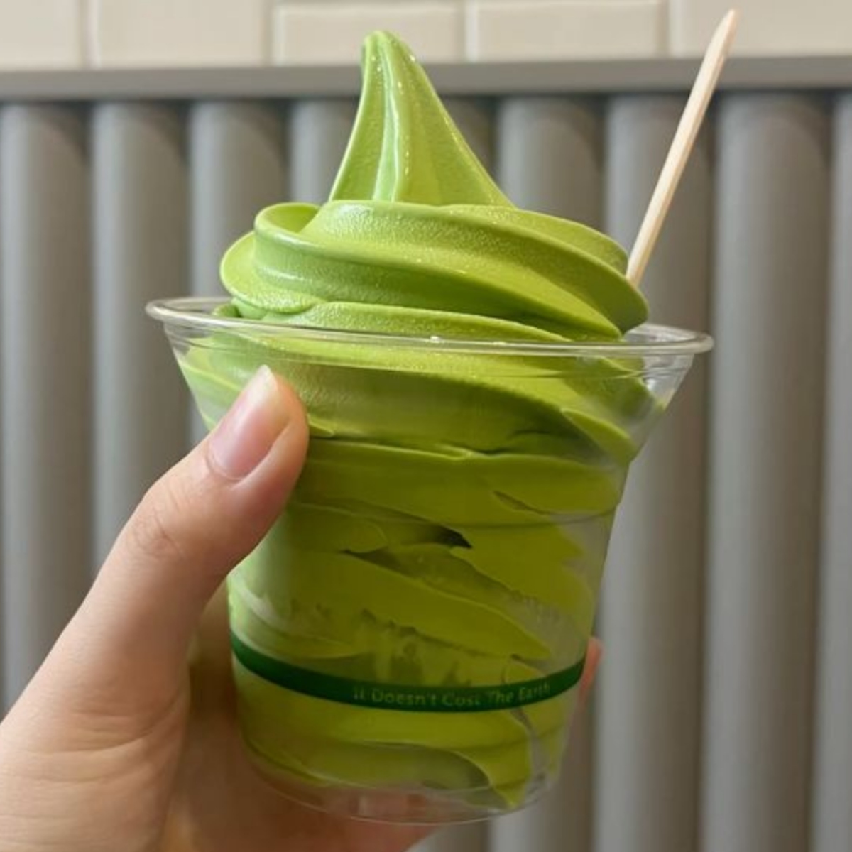 Hand holding a cup of green matcha soft serve ice cream with a small spoon