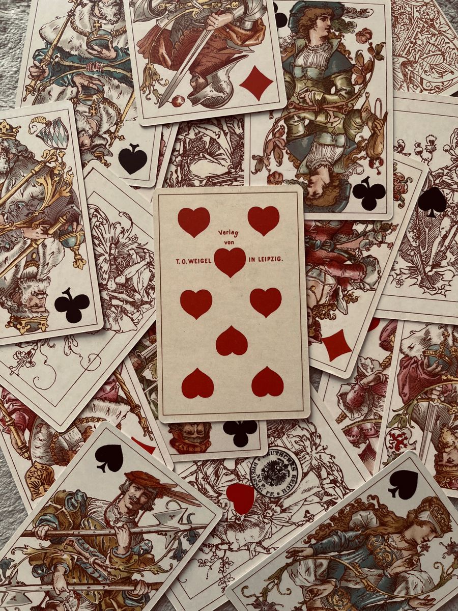 Pile of ornate vintage playing cards with detailed illustrations, Nine of Hearts centered on top