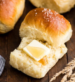 Soft bread roll opened with a pat of butter on a wooden table