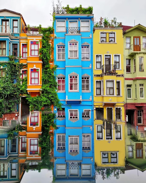 Colorful waterfront houses with ornate facades reflected in calm water, featuring blue, yellow, and orange buildings