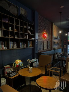 Dim cafe interior with round wooden tables, chairs, bookshelves, and a red neon sign