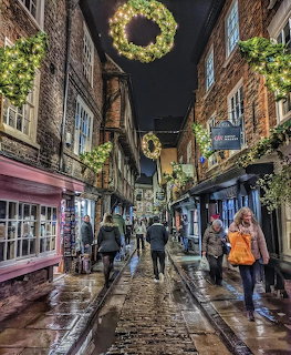Narrow Yorkshire street at night with Christmas wreaths, wet cobblestones, old buildings, and people walking