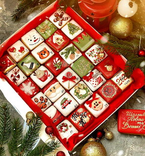 Red box of assorted Christmas chocolates decorated with festive designs, gold ornaments and pine branches nearby