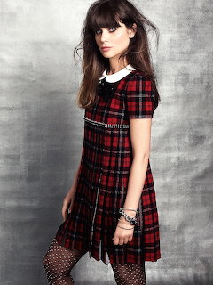 Studio portrait of Zooey Deschanel wearing a red plaid dress against a gray background