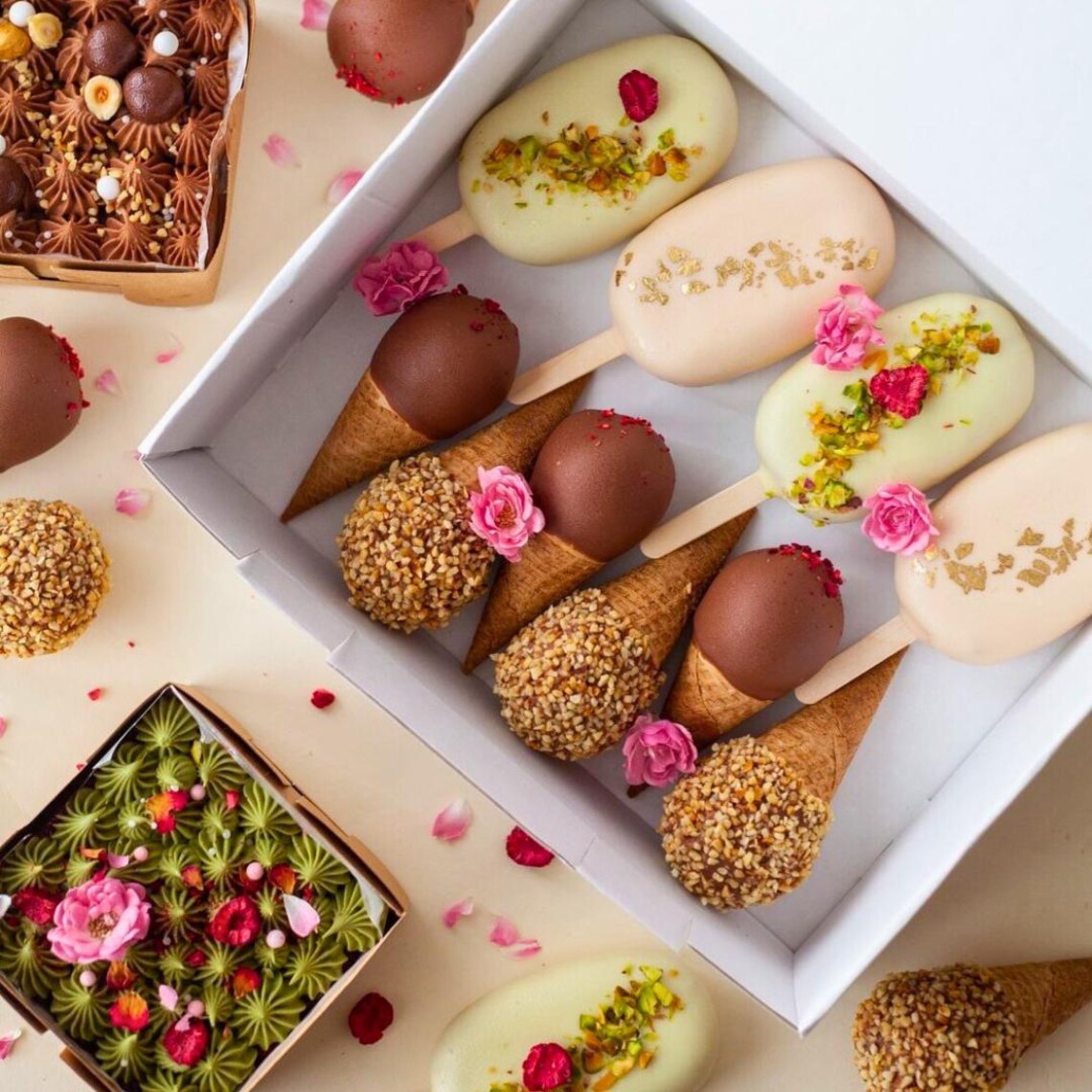 Assorted cake pops with chocolate coating, sprinkles, nuts, and edible flowers on white tray