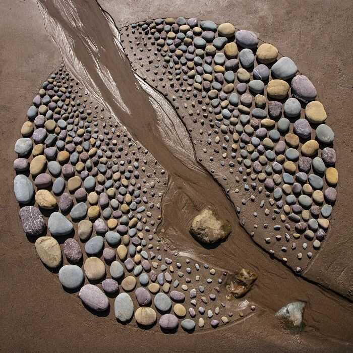 Circular pebble artwork on wet sand with a narrow stream flowing through it