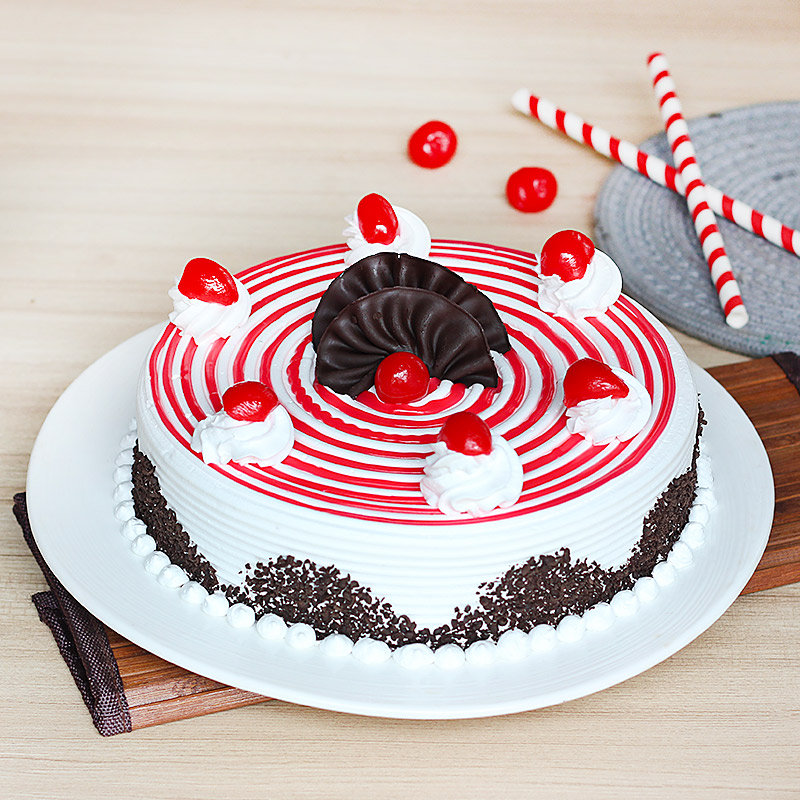 Round strawberry cake with red spiral icing, whipped cream, cherries, and chocolate decoration on a plate