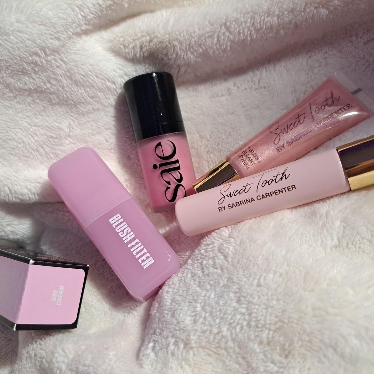 Pink makeup products including lip gloss, concealer and blush on white fur texture