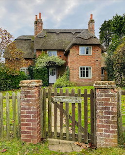 Brick cottage with thatched roof behind wooden gate and brick pillars