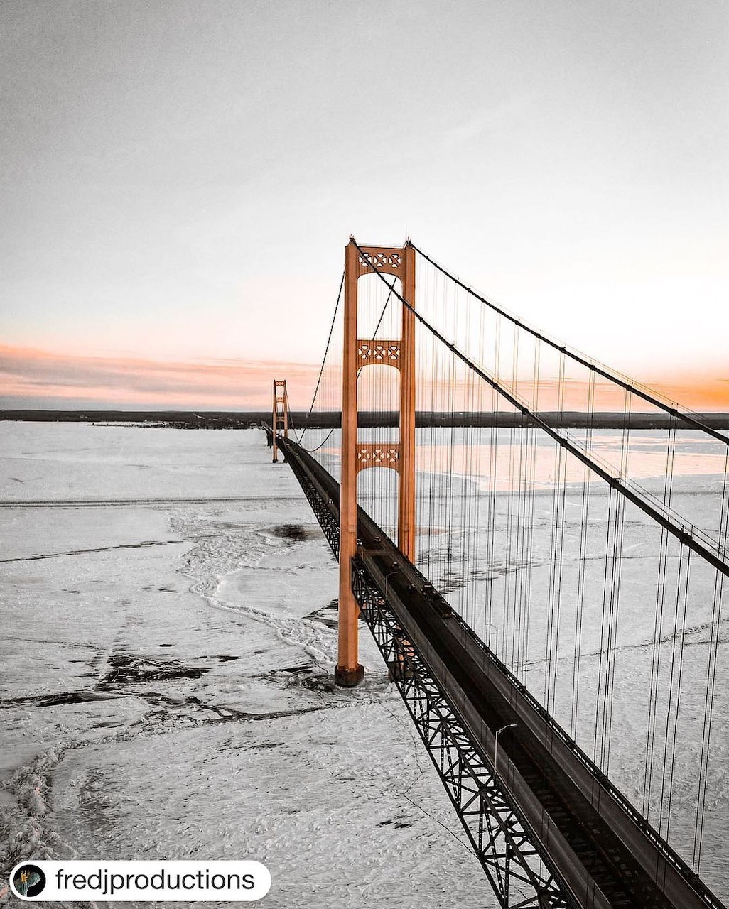 Aerial view of orange suspension bridge over water at sunset