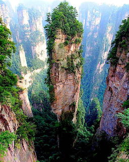 Tall sandstone rock pilar topped with green trees surrounded by misty cliffs in Zhangjiajie, China