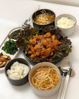 Top-down Korean meal with spicy chicken, rice, bean sprout soup, lettuce, and side dishes