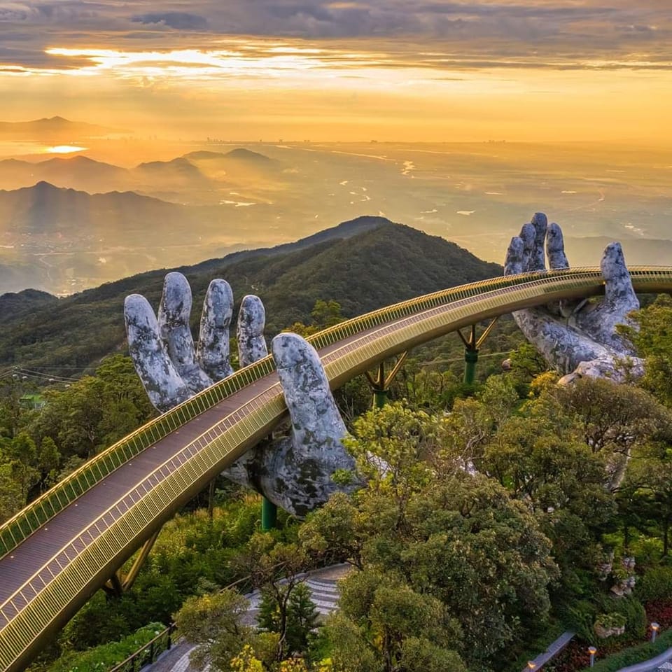 Golden Bridge in Vietnam supported by giant stone hands above a forested mountain landscape at sunset