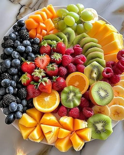 Overhead view of a colorful assorted fruit platter with berries, kiwi, citrus, mango, and grapes on a white plate.