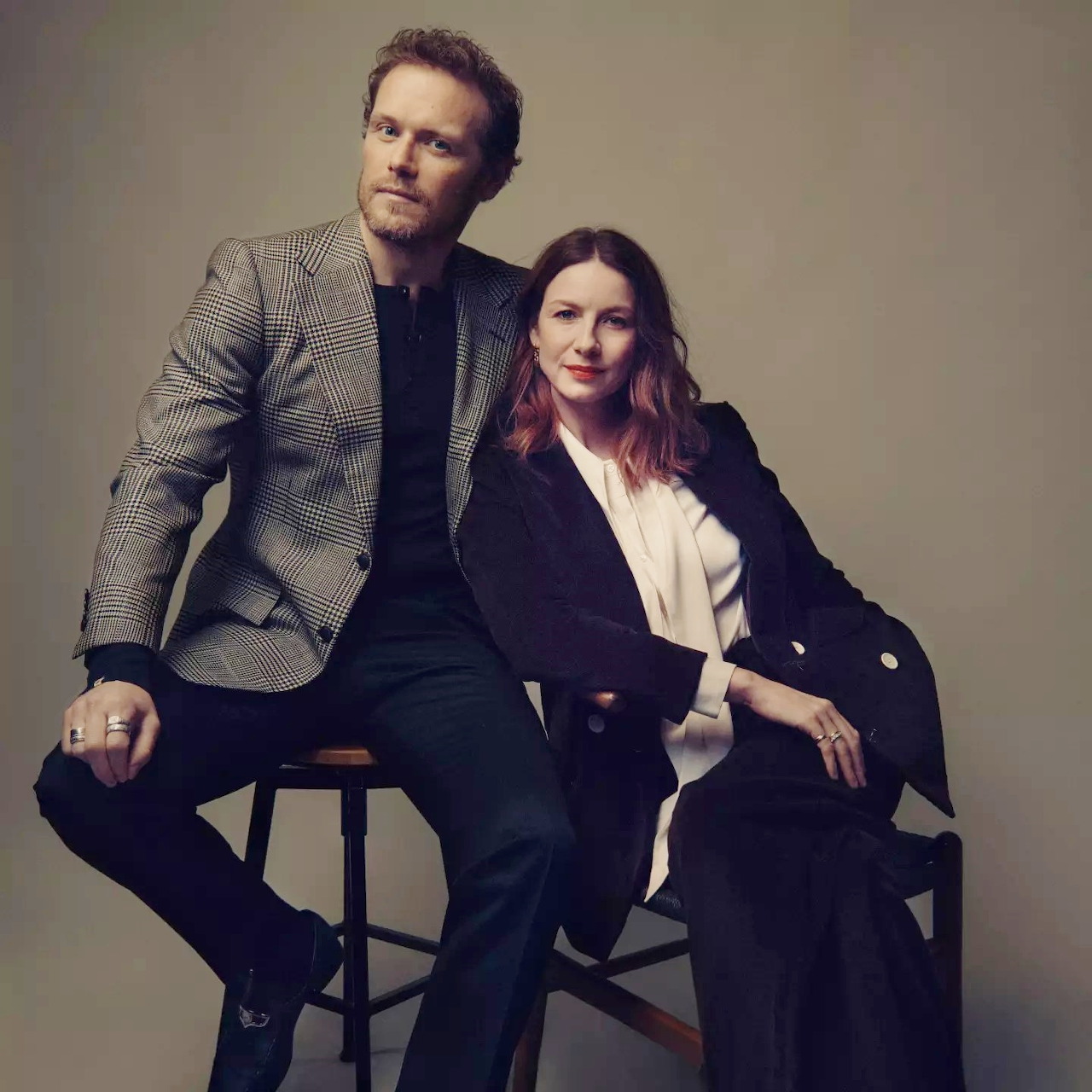 Man and woman in formal business wear seated on stool in studio portrait