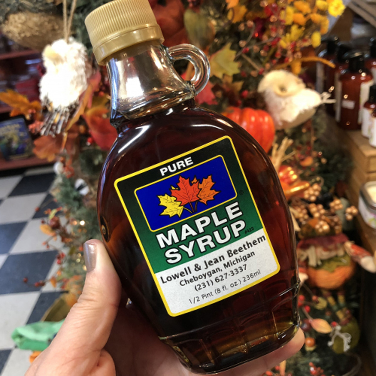 Hand holding maple syrup bottle with fall decor behind