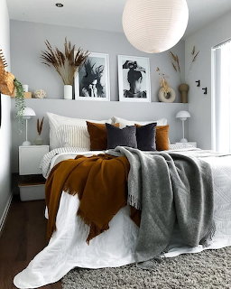 Cozy bedroom with brown and grey pillows, rust throw blanket, pampas grass, and framed wall art