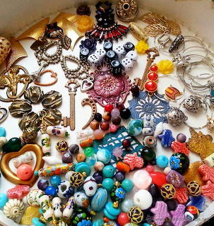 Colorful mixed beads, charms, keys, chains, and jewelry pieces scattered on a white background.