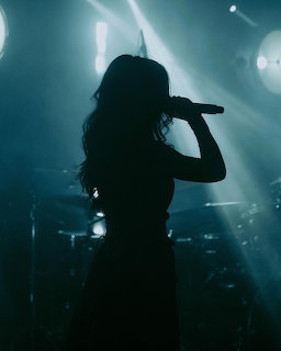 Silhouette of a female singer holding a microphone on a dark stage with bright lights