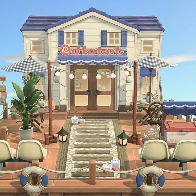 Stylized seaside hotel entrance with patio seating, umbrellas, and lifebuoys