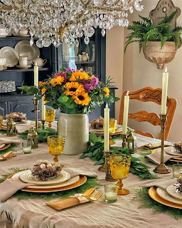 Elegant dinner table with sunflower centerpiece, candles, amber glasses, and green foliage decor