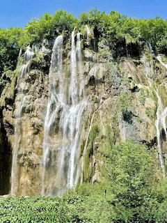 Waterfalls flowing down a rocky cliff with green trees and blue sky