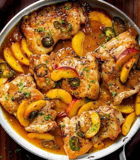 Skillet with chicken pieces, peach slices, jalapeños, and herbs in a savory sauce